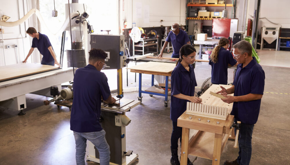 Carpenters Working On Machines In Busy Woodworking Workshop